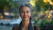 © ProPhotos - A gray-haired woman smiling at the camera with a fountain and a picturesque park in the background.