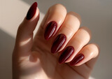 Glossy burgundy nails with almond shape in soft light