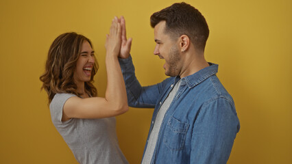 Man and woman joyfully high-fiving against a vivid yellow background, symbolizing friendship, team spirit, and positive interaction in a bright setting.