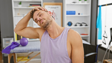 Sticker - A young hispanic man with a beard stretching his neck in a rehabilitation clinic setting, conveying health and wellness.