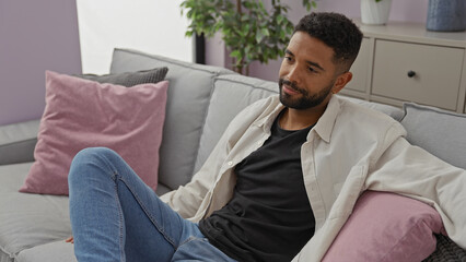 Wall Mural - Relaxed african american man with beard sitting in a modern living room apartment