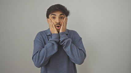 Canvas Print - Surprised young man with beard against white background expressing shock with hands on face