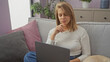 © Krakenimages.com - A contemplative young woman sits indoors with her laptop and pet dog beside her on a cozy couch in a well-decorated room.