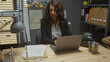 © Krakenimages.com - Mature hispanic woman working on laptop in a detective's office filled with files and a map.