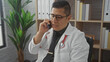 © Krakenimages.com - Young hispanic man in a white lab coat talking on the phone in a clinic office