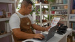 © Krakenimages.com - Young man in apron working on laptop and analyzing documents in a bakery shop with shelves of products in the background