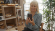 © Krakenimages.com - Beautiful blonde woman in a cozy bakery shop, smiling while looking at her phone inside a bright, indoor setting with baked goods displayed around.