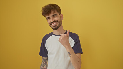 Smiling bearded young hispanic man giving a thumbs up against a vibrant yellow background