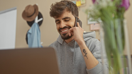 Wall Mural - Bearded hispanic man smiling in apartment while talking on smartphone