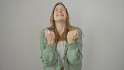 Smiling blonde woman in green sweater with clenched fists conveying excitement against a white background