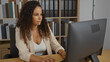 © Krakenimages.com - Young woman with curly hair working in an office with shelves in the background, focused on computer screen