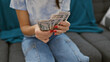 © Krakenimages.com - A young woman counts dollars on a sofa in a cozy indoor home setting.