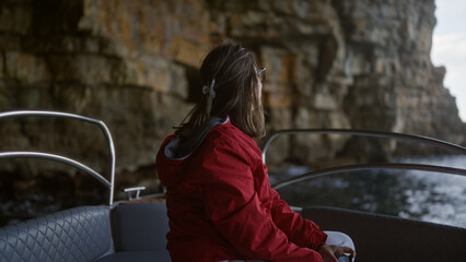 Young hispanic woman on a boat exploring a stunning cove in polignano a mare, puglia, italy, with rocky cliffs and clear sea waters in the background.