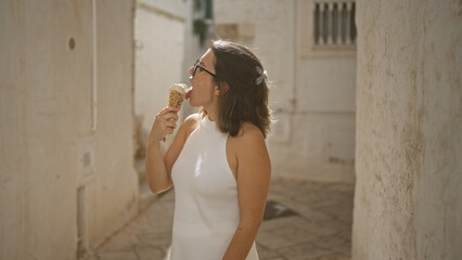 Wall Mural - A beautiful young hispanic woman enjoys an ice cream in the charming white-washed streets of the old town in locorotondo, puglia, italy.