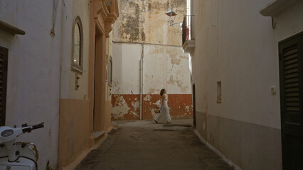 Poster - A young woman walks through the picturesque streets of gallipoli in puglia, italy, showcasing the charm of old european architecture.