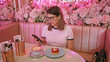 © Krakenimages.com - Adult woman checks phone in pink floral cafe with coffee and dessert on table