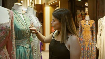 Wall Mural - A young woman examines traditional dresses at a souk in dubai, portraying a tourist exploring local culture.