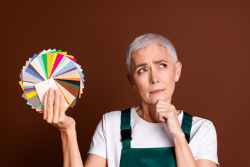 Poster - Photo of minded dreamy charming senior woman wear uniform hold palette look empty space isolated on brown color background