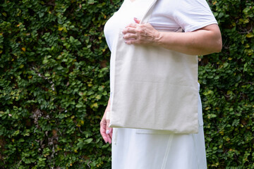 Wall Mural - Close up of woman holding eco or reusable shopping bag against green leaves background