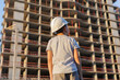 © Studio Peace - Little boy in a protective helmet looks at the construction of a multi-storey building at sunset.