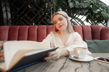 Dreamy young womanreding her notes in diary resting in cozy cafe