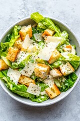 A bowl of fresh Caesar salad with crispy romaine lettuce, croutons, and a creamy dressing, topped with shaved Parmesan