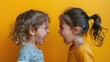 © andriyyavor - Two children, one with curly hair and the other with a ponytail, loudly yelling at each other against a vivid yellow backdrop, representing a fierce argument or play fight.