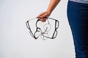 Person holding multiple pairs of glasses in a bright indoor setting. A person grips several pairs of glasses in their hand