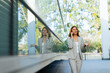 © BGStock72 - Confident business woman enjoying a sunny day outdoors while browsing her phone near modern architecture surrounded by nature
