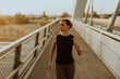 © BGStock72 - Determined runner jogs along a sunlit bridge during the golden hour, blending fitness and serenity in an urban landscape