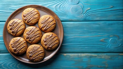 Round oatmeal cookies covered with milk chocolate and icing on a blue plate top view