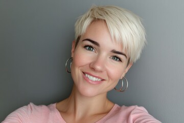 Smiling woman with blonde short hair and hoop earrings against gray background