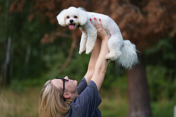 Portrait of smiling young woman kiss dog in Natural Park. Dog lover woman wearing blue dress with dog during good day. Concept of friendship and beautiful girl with a small dog