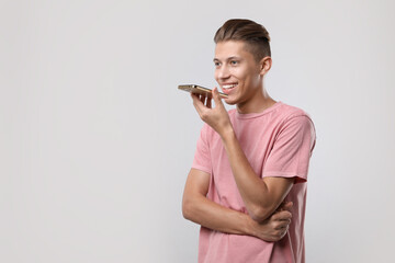 Poster - Young man recording voice message via smartphone on light gray background, space for text