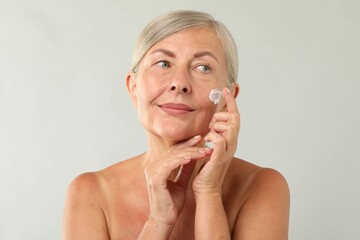 Canvas Print - Senior woman applying face cream on light background