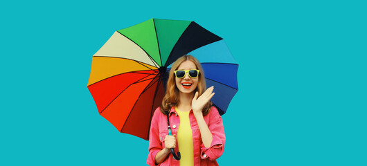 Poster - Stylish happy smiling young woman holding colorful umbrella, cheerful girl on bright blue background