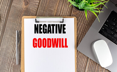 Clipboard with the text negative goodwill on a wooden desk, next to a pen, laptop, mouse, and plant