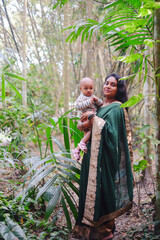 Wall Mural - South asian young lady with a traditional costumes holding her baby boy in a garden 