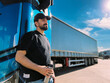 © Anna - A young man is a professional driver near a blue truck. A handsome guy, a transportation worker stands next to a large truck car