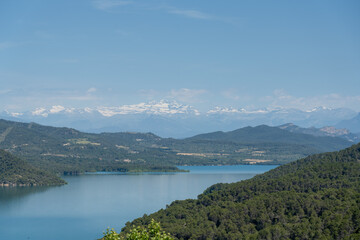 view over beautiful water, hills and distant Pyrenees mountains at Embalse de El Grado Reservoir, blue summer sky, Huesca, Spain