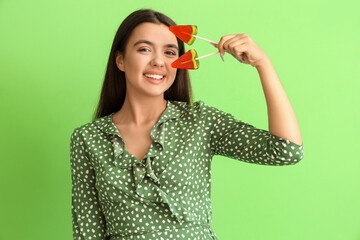 Poster - Beautiful happy young woman with watermelon lollipops on green background