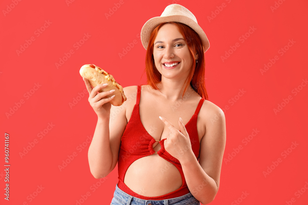 Beautiful young woman with hot dog on red background