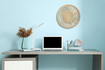 Poster - Stylish workplace with modern laptop, books and lamp near blue wall in office