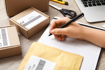 Sticker - Female postal worker with package writing in notebook on table, closeup