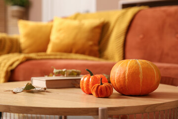 Wall Mural - Pumpkins with autumn leaves and book on coffee table in stylish living room, closeup