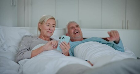 Wall Mural - Mature couple, bed and phone with laughing, morning and news app with commitment. Talking, social media and health relationship in home with discussion together in bedroom with happy people and love