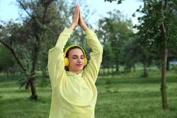 Wall Mural - Sporty young woman with headphones doing yoga in park