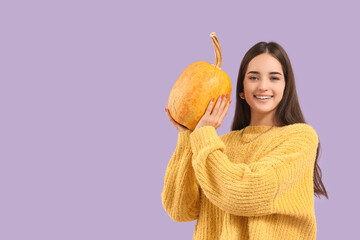 Beautiful young happy woman with pumpkin on purple background