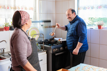 Senior couple sharing, cooking and frying sweet pastry biscuits in their traditional domestic kitchen