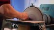 © DC Studio - Woodworker shaping wooden bowl on disc sander in carpentry shop, showcasing precision. Cabinetmaker working in joinery, guiding wood against grinding machine rotating disc, camera A close up
